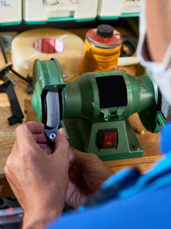 Hands shaping a part on a bench grinder at a workbench
